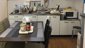 A compact kitchen with a dining table, microwave, and cabinets. - Minshuku Warakuya (Kobayashi)
