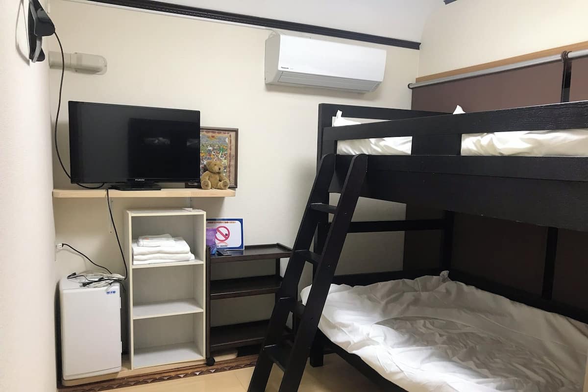 Habitación con literas, televisión, un refrigerador pequeño, un estante con ropa doblada y un cartel de no fumar.