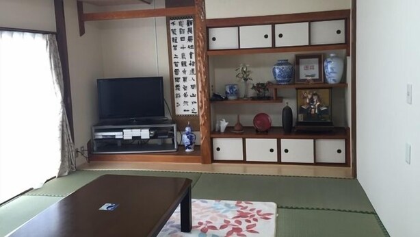 A traditional Japanese room with tatami flooring, a television, a cabinet with decorative items, and a shoji screen. - Minshuku Warakuya (Kobayashi)