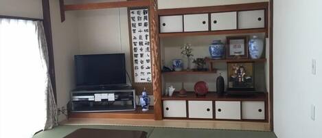 A traditional Japanese room with tatami flooring, a television, a cabinet with decorative items, and a shoji screen.