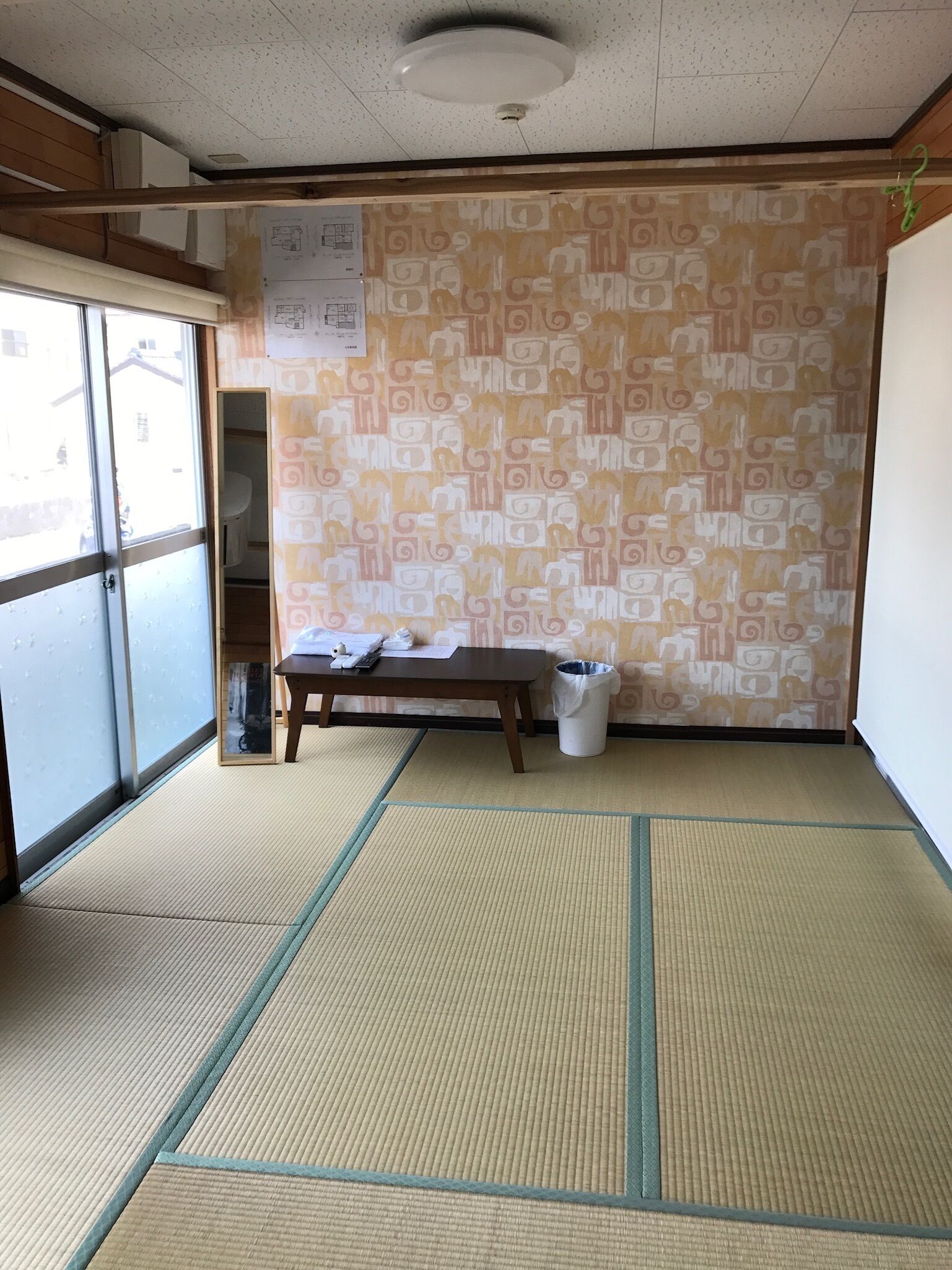 Una habitación con suelo de tatami, una mesa de madera, un cesto de basura y una pared con diseño.