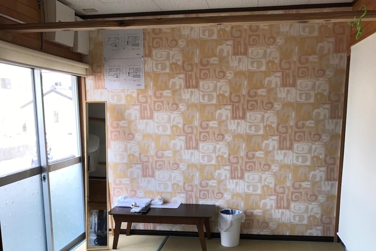 Una habitación con suelo de tatami, una mesa de madera, un cesto de basura y una pared con diseño.