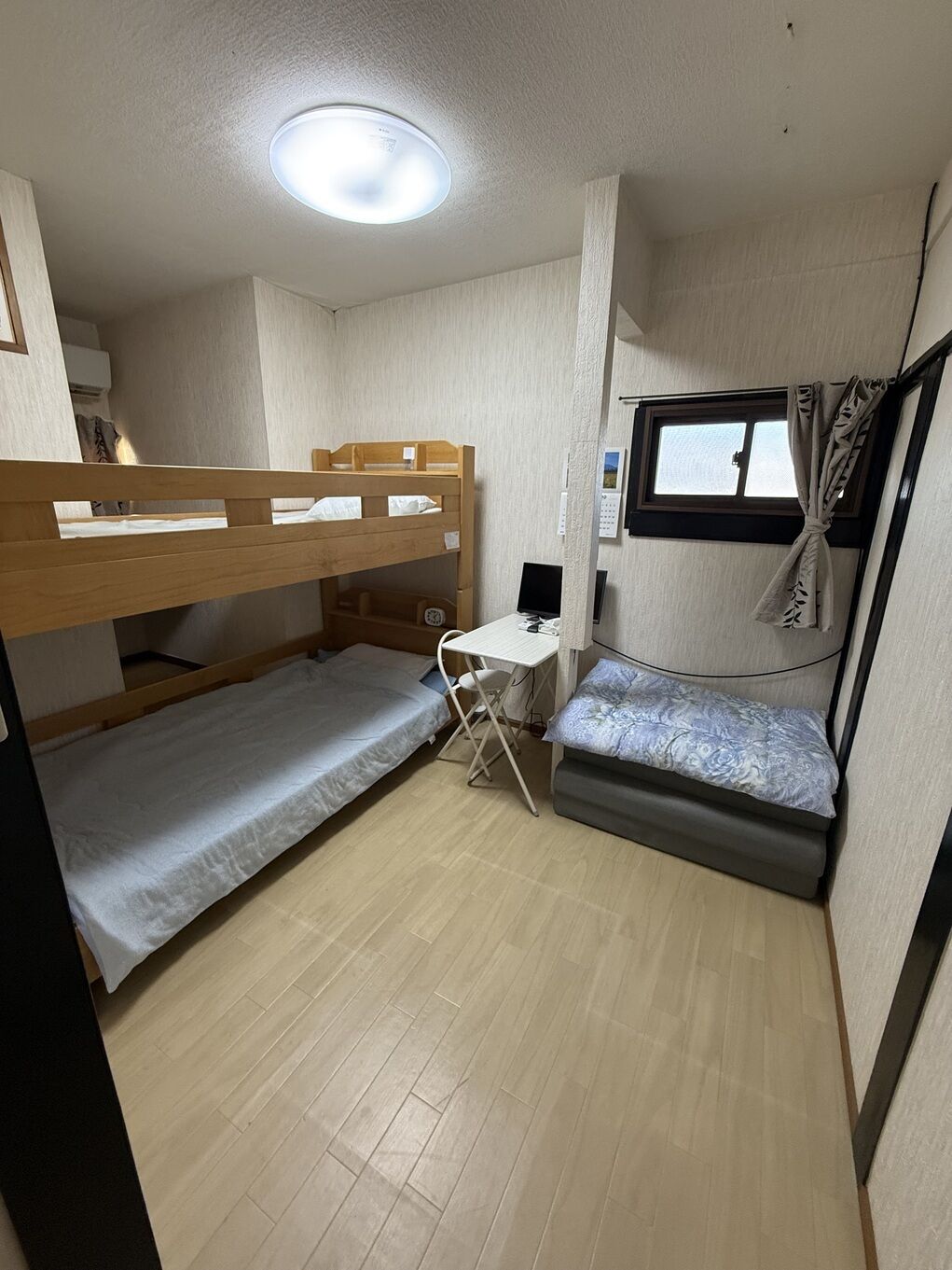 Habitación compacta con literas, un escritorio, una silla, un ventanal pequeño y una lámpara en el techo.