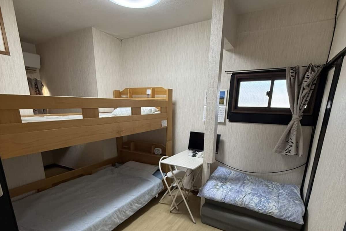 Habitación compacta con literas, un escritorio, una silla, un ventanal pequeño y una lámpara en el techo.
