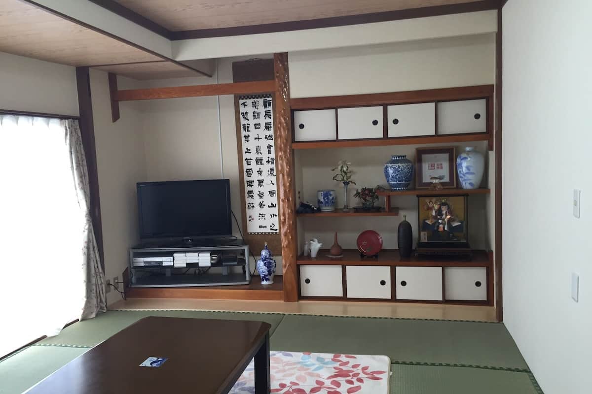 Una habitación japonesa tradicional con suelo de tatami, televisor, aparador con adornos y un shoji con caligrafía.