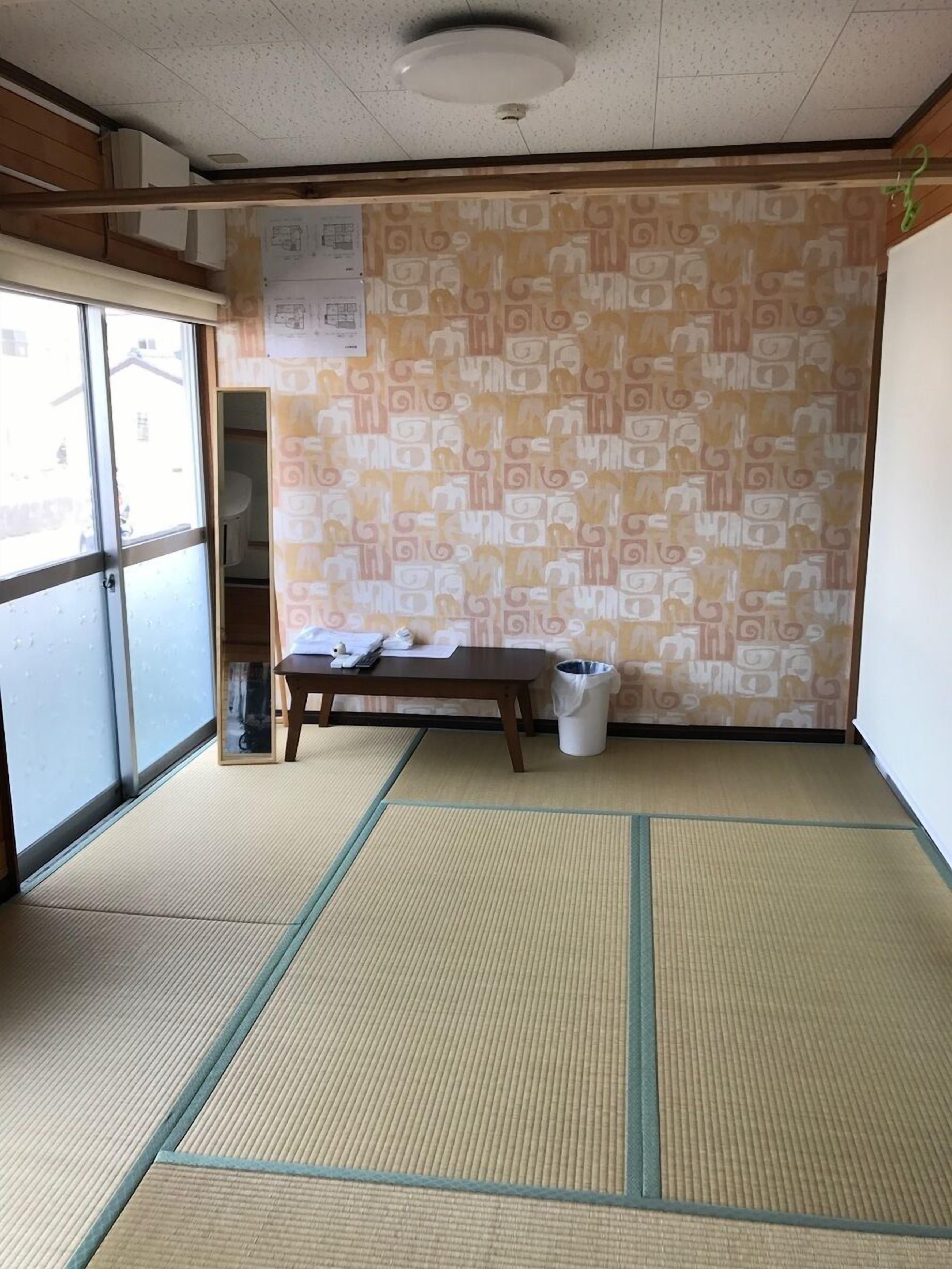 Una habitación con suelo de tatami, una mesa de madera, un cubo de basura y un muro estampado.
