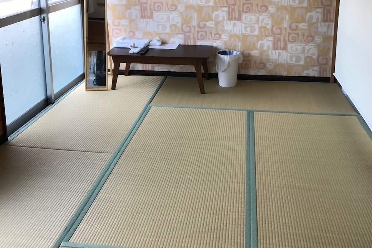 Una habitación con suelo de tatami, una mesa de madera, un cubo de basura y un muro estampado.