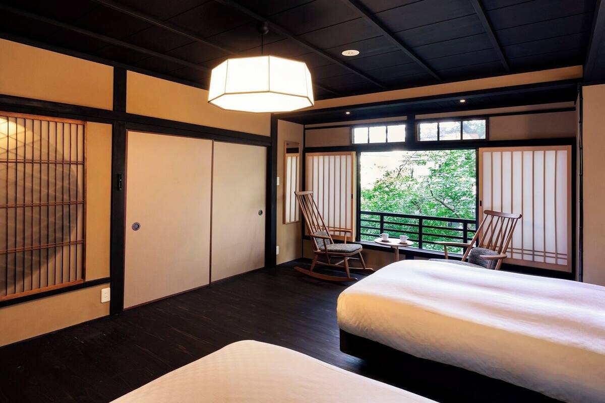 Una habitación tradicional japonesa con suelo de tatami, una cama, una mecedora y un balcón con vistas.