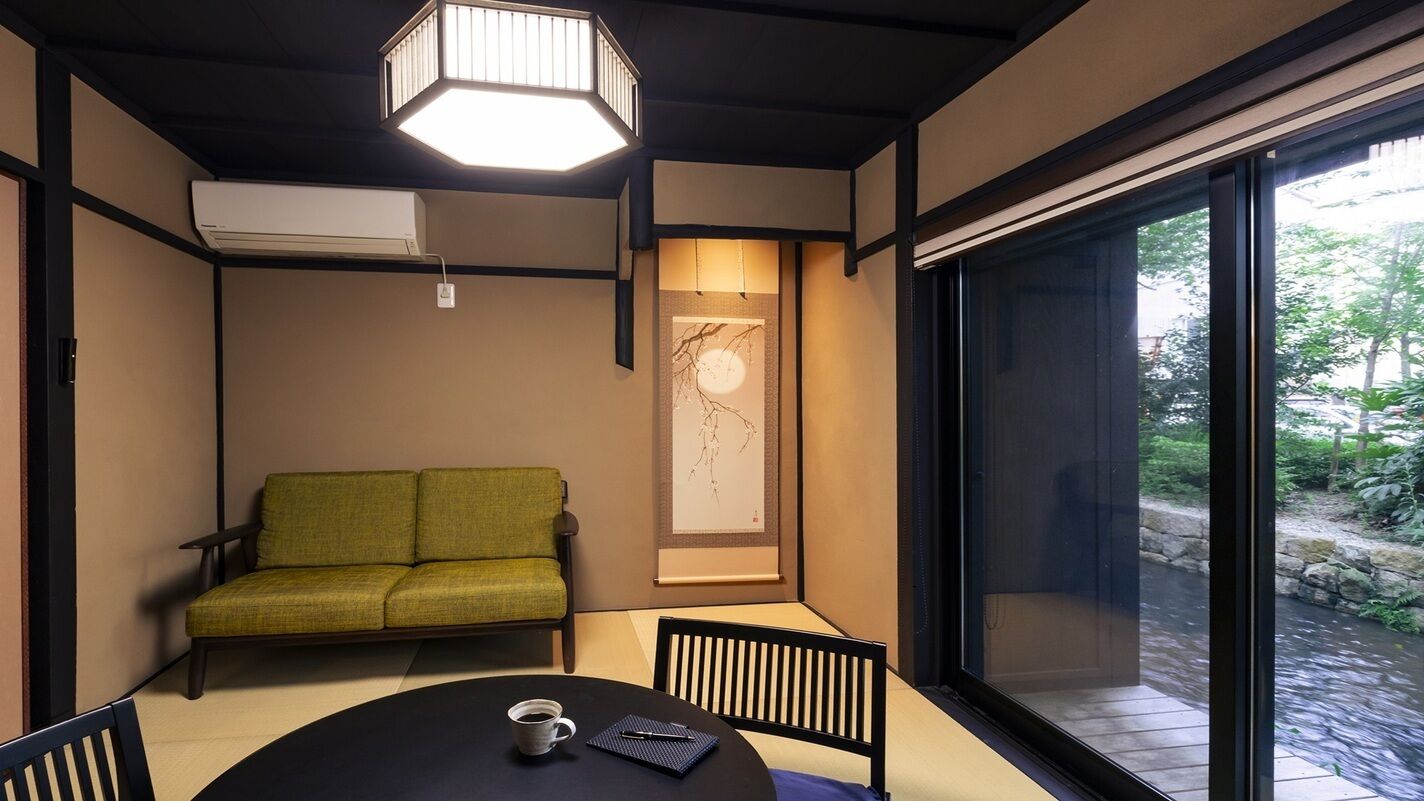A room with a sofa, a table with a cup and a book, a large window, and a ceiling light fixture.