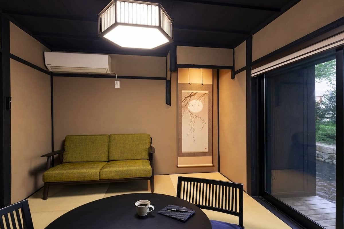 A room with a sofa, a table with a cup and a book, a large window, and a ceiling light fixture.