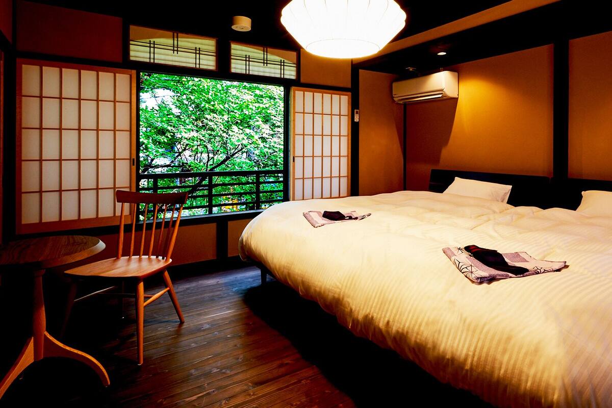 Habitación de hotel con cama, una silla, un ventanal con vistas a zonas verdes y un tradicional divisor corredizo japonés.