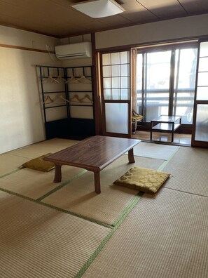 A traditional Japanese room with tatami flooring, a wooden table, a bench, a hanging clothes rack, and a sliding door with a view. - Monzenya (Tokoname)