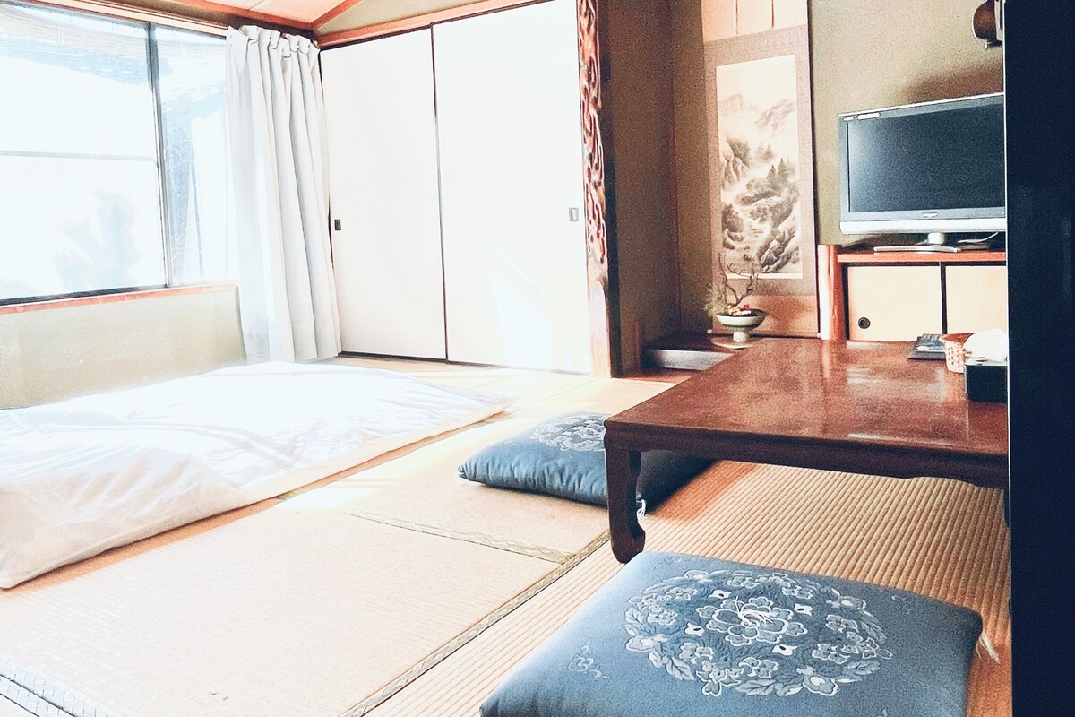 A room with tatami mats, a bed, a television, and a sliding door.