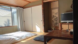 A traditional Japanese-style room with tatami flooring, a bed with white bedding, a television, and a sliding door. - Monzenya (Tokoname)