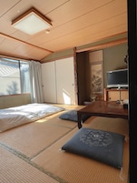 A traditional Japanese-style room with tatami flooring, a bed with white bedding, a television, and a sliding door.