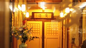 A corridor with a wooden floor, a vase with flowers on a table, and two doors with a sign above them. - Tsutaya Ryokan (Kuji)
