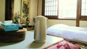 A hotel room with a bed, a table with a kettle, a tissue box, and a decorative item. - Tsutaya Ryokan (Kuji)