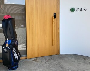 A wooden door with a keyhole and a small electronic lock, a black and blue bag with 'St. Andrews' on it, and a wall with Japanese characters and a green circular design. - Farmstay Miyuki-dori Goen (Ukiha)