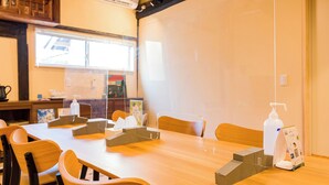 Uma sala de conferências com uma mesa comprida, cadeiras, um quadro branco e uma janela com persianas.