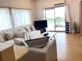 Una sala de estar moderna con un sofá, una mesa de centro, un televisor y un ventanal corredero que da a un espacio exterior.