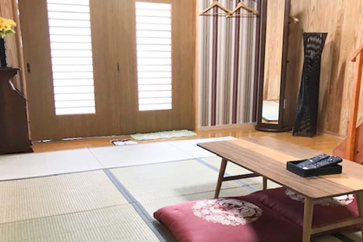 A traditional Japanese room with tatami flooring, a low table, a cushion, a hanging wardrobe, and a sliding door.