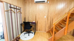 A room with a wooden floor, a black office chair, a small table, a white rug, a wooden staircase, and a striped curtain. - Matsue no Sato (Matsue)