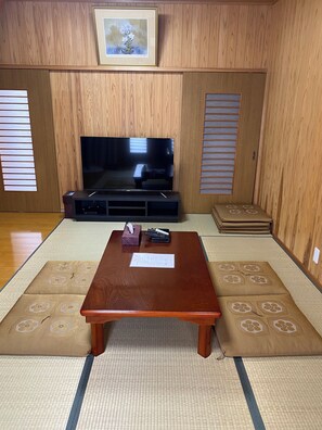 A traditional Japanese room with tatami flooring, a television, a table, and a futon. - Matsue no Sato (Matsue)
