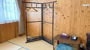 A room with a tatami mat floor, a wooden wardrobe, a small table with a tissue box and a phone, and a hanging rack with clothes. - Matsue no Sato (Matsue)