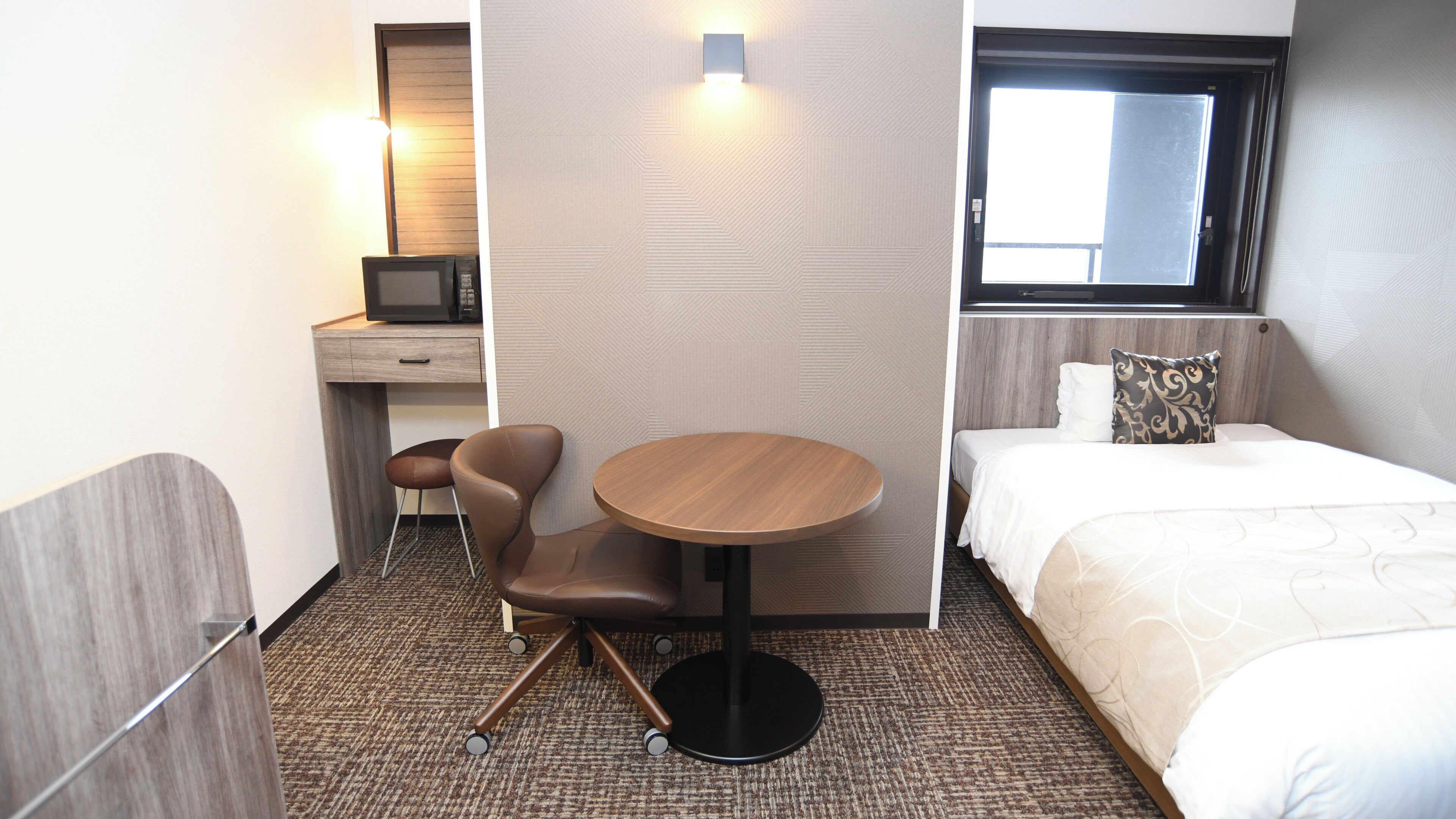 Quarto de hotel com cama, escrivaninha com cadeira, mesa redonda e televisão.