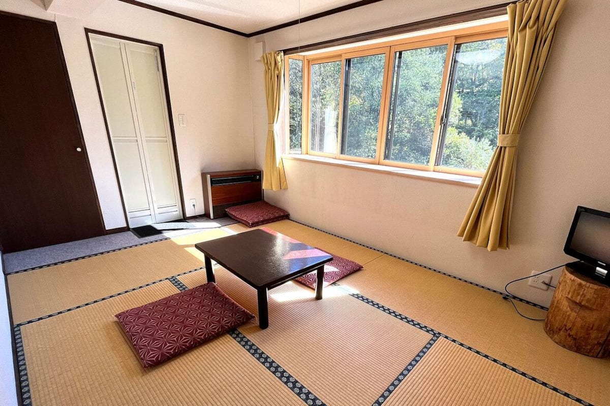 A room with tatami flooring, a low table, a TV, and a window with curtains.