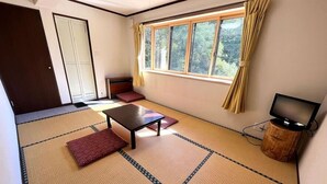 A room with tatami flooring, a low table, a sofa, a TV on a wooden stand, and a sliding door. - Tairappyouchaya (Yuzawa)