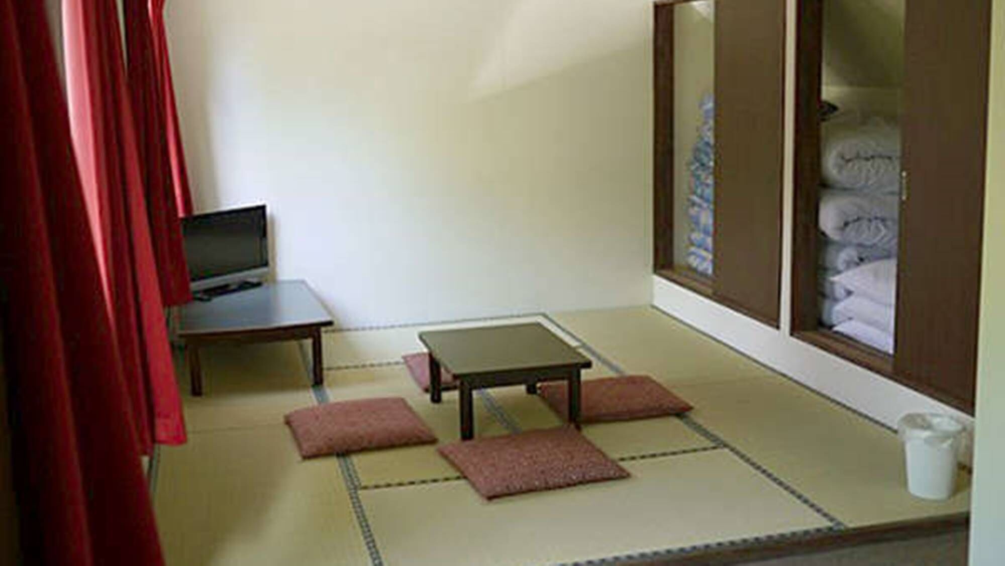 A room with tatami flooring, a small table, a television, and a cabinet with folded items.
