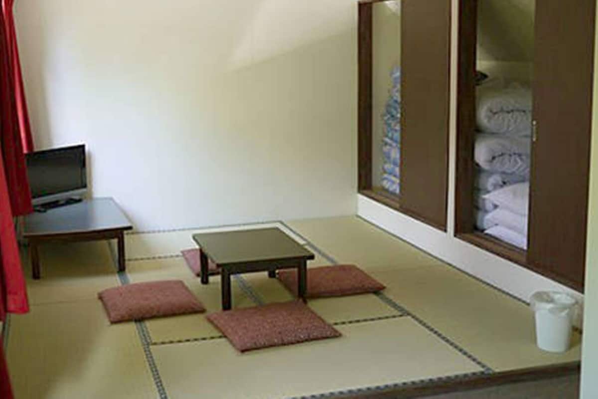 A room with tatami flooring, a small table, a television, and a cabinet with folded items.