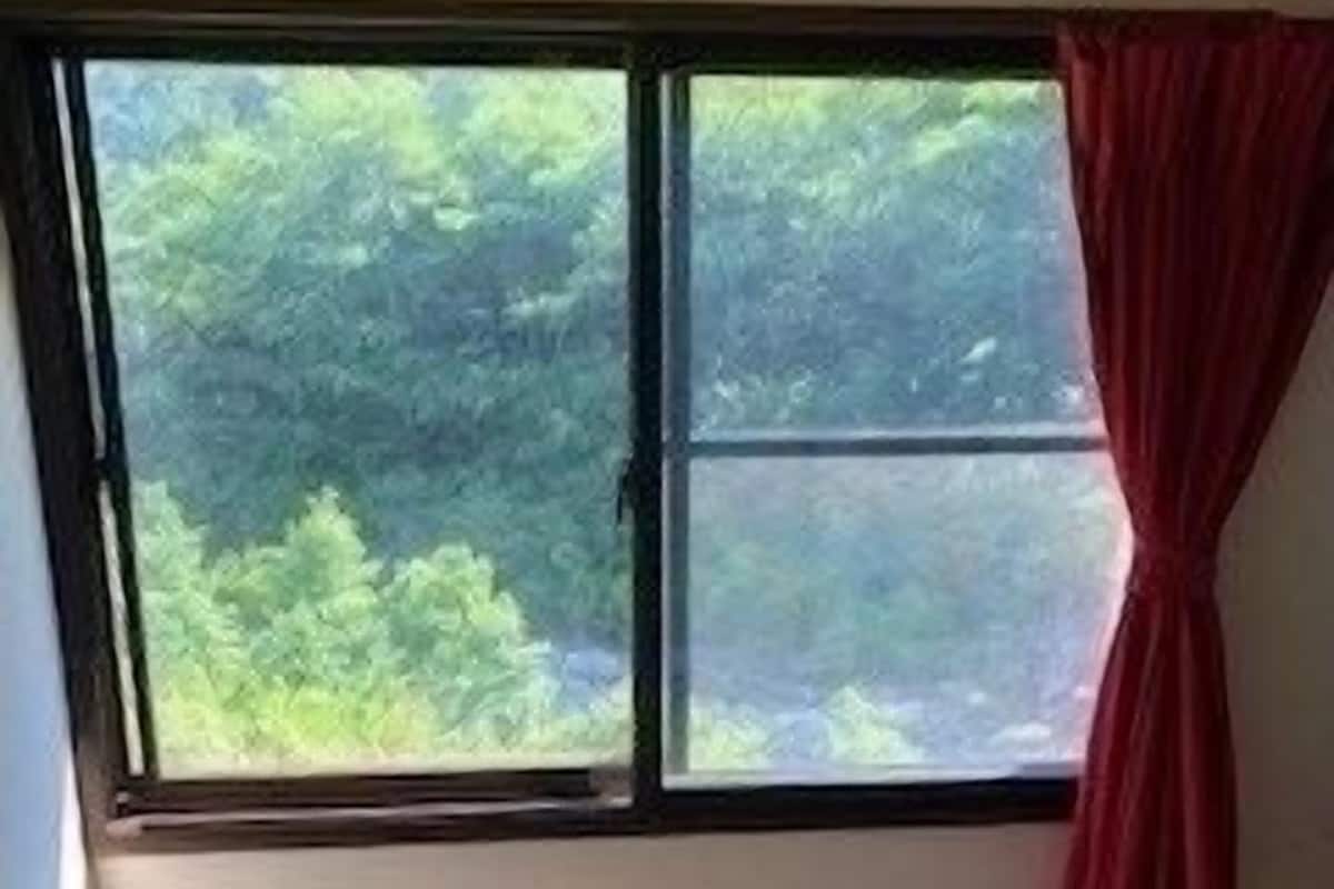 A room with tatami flooring, a window with a view of greenery, and a red curtain.
