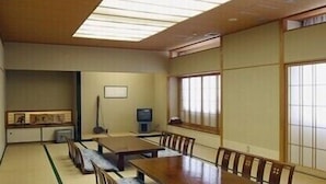 Une pièce de style japonais traditionnel, avec un sol recouvert de tatamis, une table basse entourée de chaises, un téléviseur et des portes coulissantes.