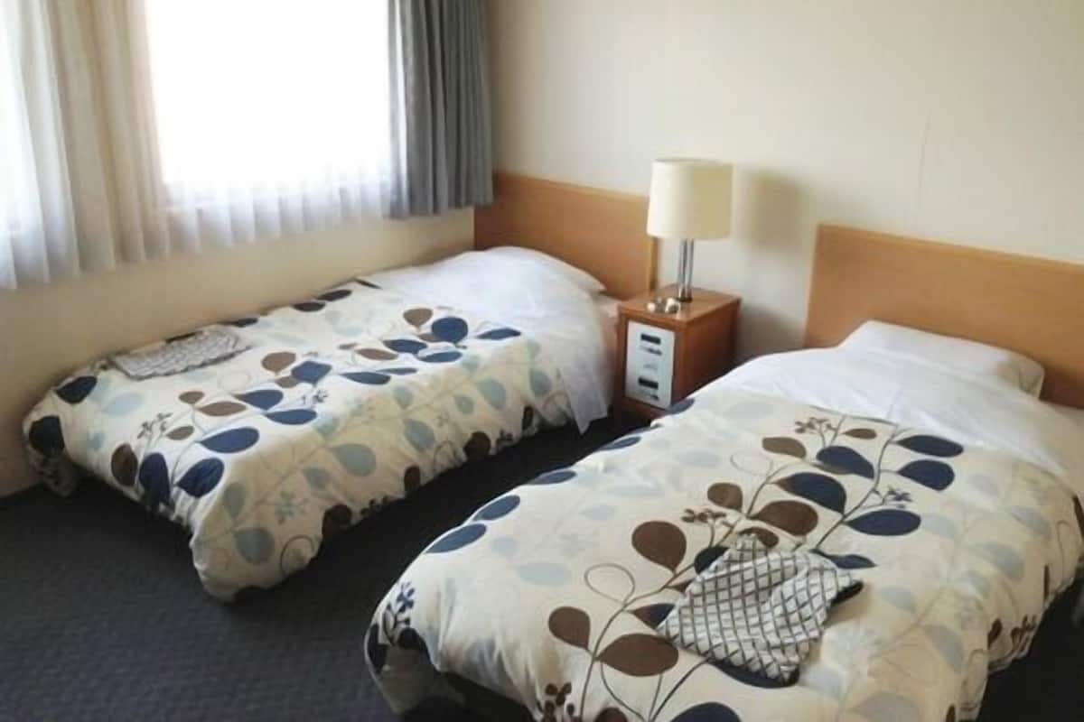 Una habitación de hotel con dos camas, una mesita de noche con lámpara y un ventanal con cortinas.