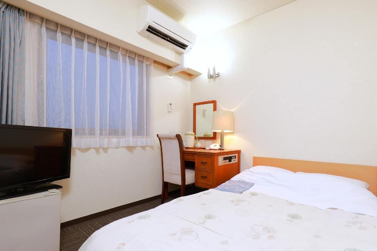 Habitación de hotel con cama, escritorio con lámpara, televisor y aire acondicionado.