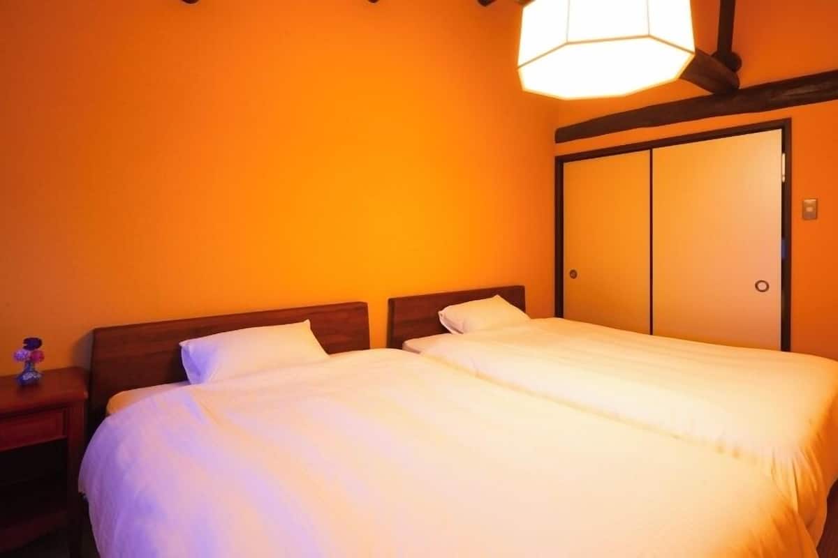 Ein Doppelbett mit weißen Leinentüchern in einem Zimmer mit orangefarbenen Wänden und einem hölzernen Kopfteil.