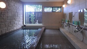 Een wellnessruimte met een groot bad, een raam met uitzicht en een douche op de muur met handzeepdispensers.