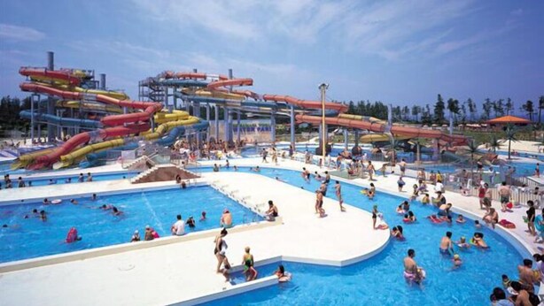 Een groot buitenzwembad met meerdere banen en een waterpark met glijbanen.
