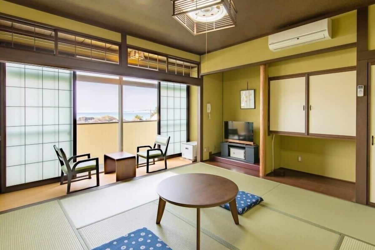Ein traditioneller japanischer Raum mit Tatami-Boden, einem niedrigen Tisch, Stühlen, einem Fernseher und Blick aufs Meer.