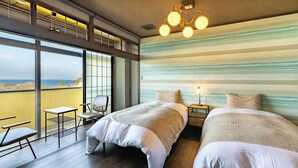 Een slaapkamer met twee bedden, een tafeltje, een stoel en uitzicht op zee.