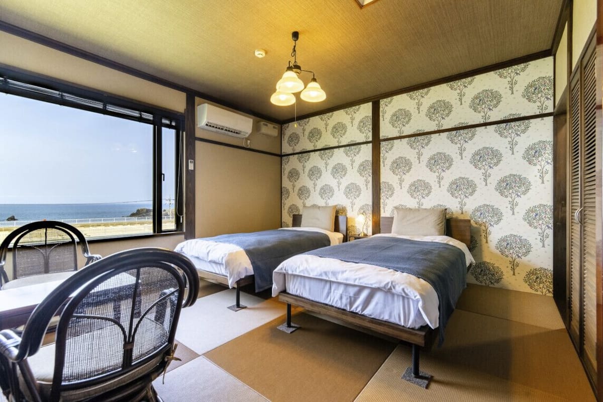 Ein Hotelzimmer mit zwei Betten, Meerblick, einem Sessel und einem Tisch.