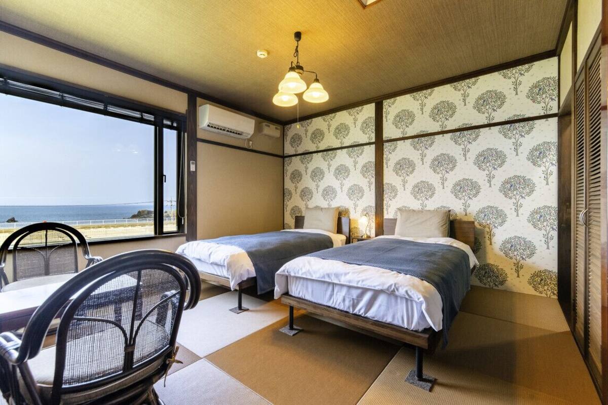 A hotel room with two beds, a view of the sea, a chair, and a table.