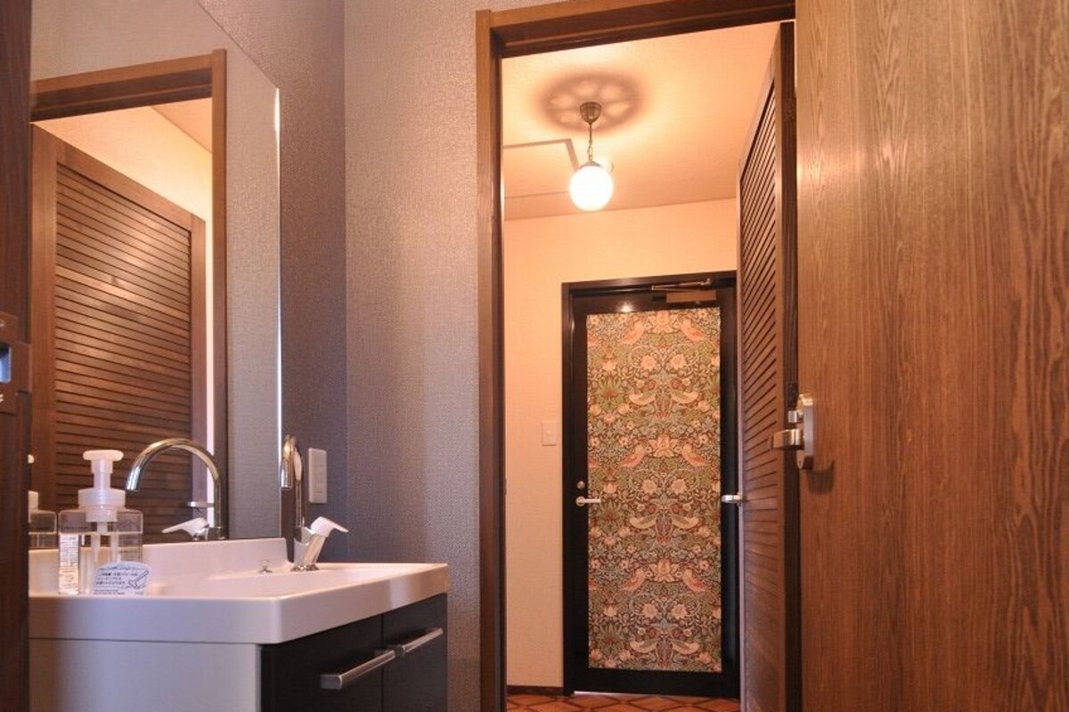 A modern bathroom with a sink, mirror, and a wooden door leading to a hallway.