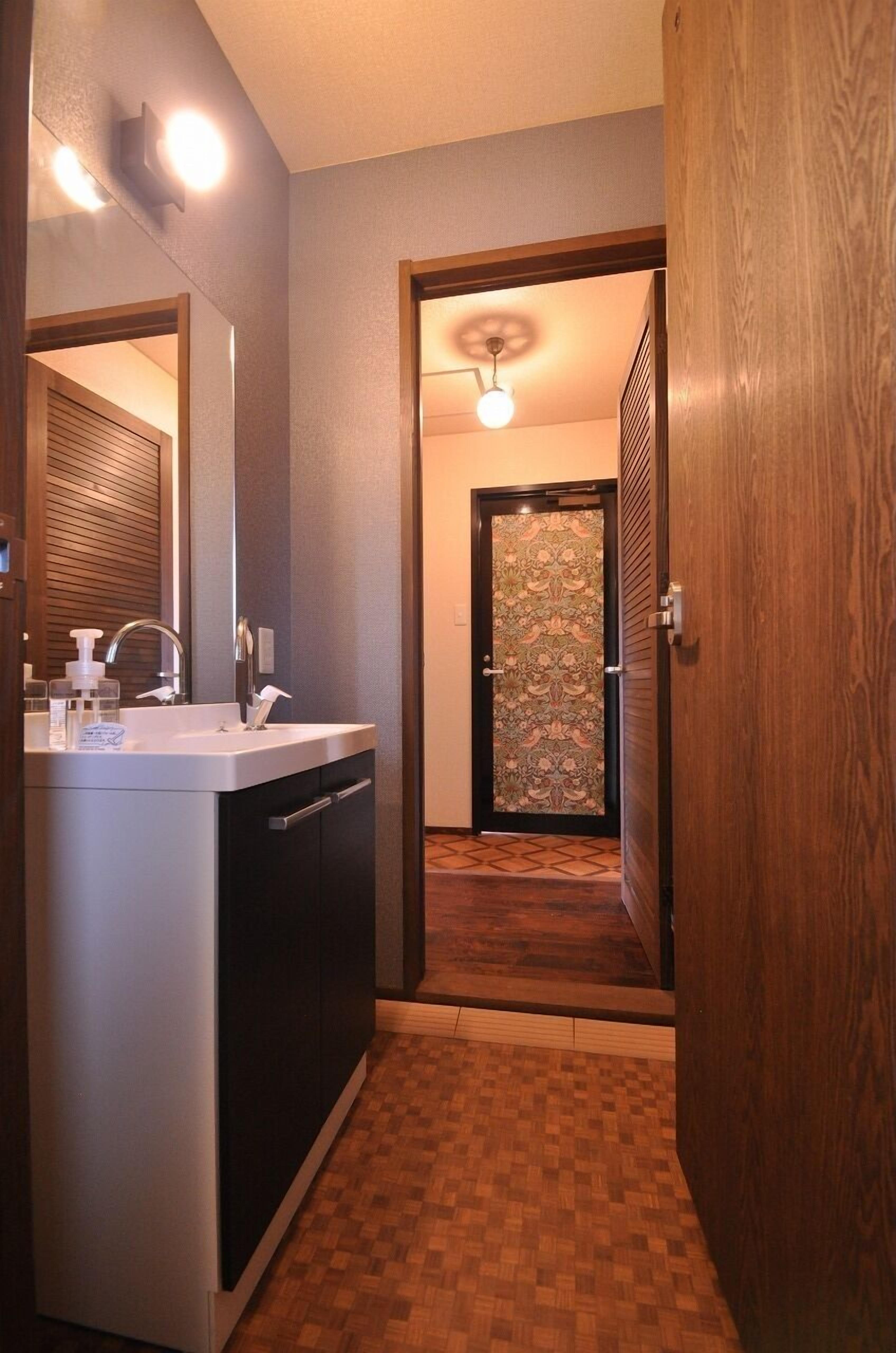 A modern bathroom with a sink, mirror, and a wooden door leading to a hallway.