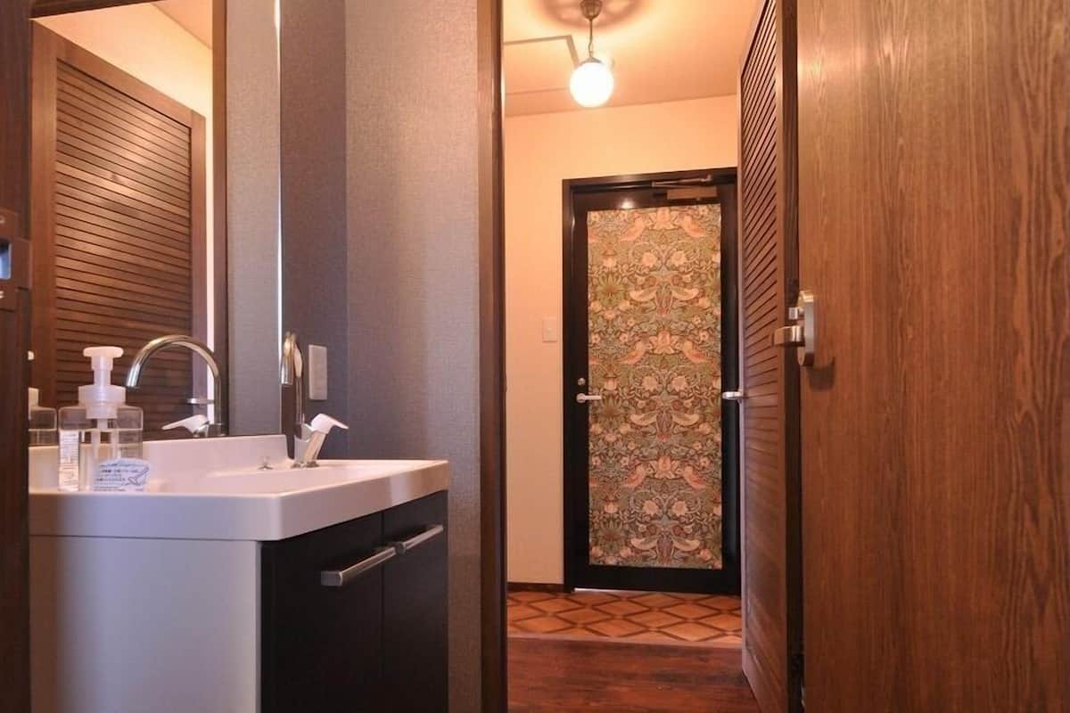 Ein modernes Badezimmer mit Waschbecken, Spiegel und einer Holztür, die zu einem Flur führt.