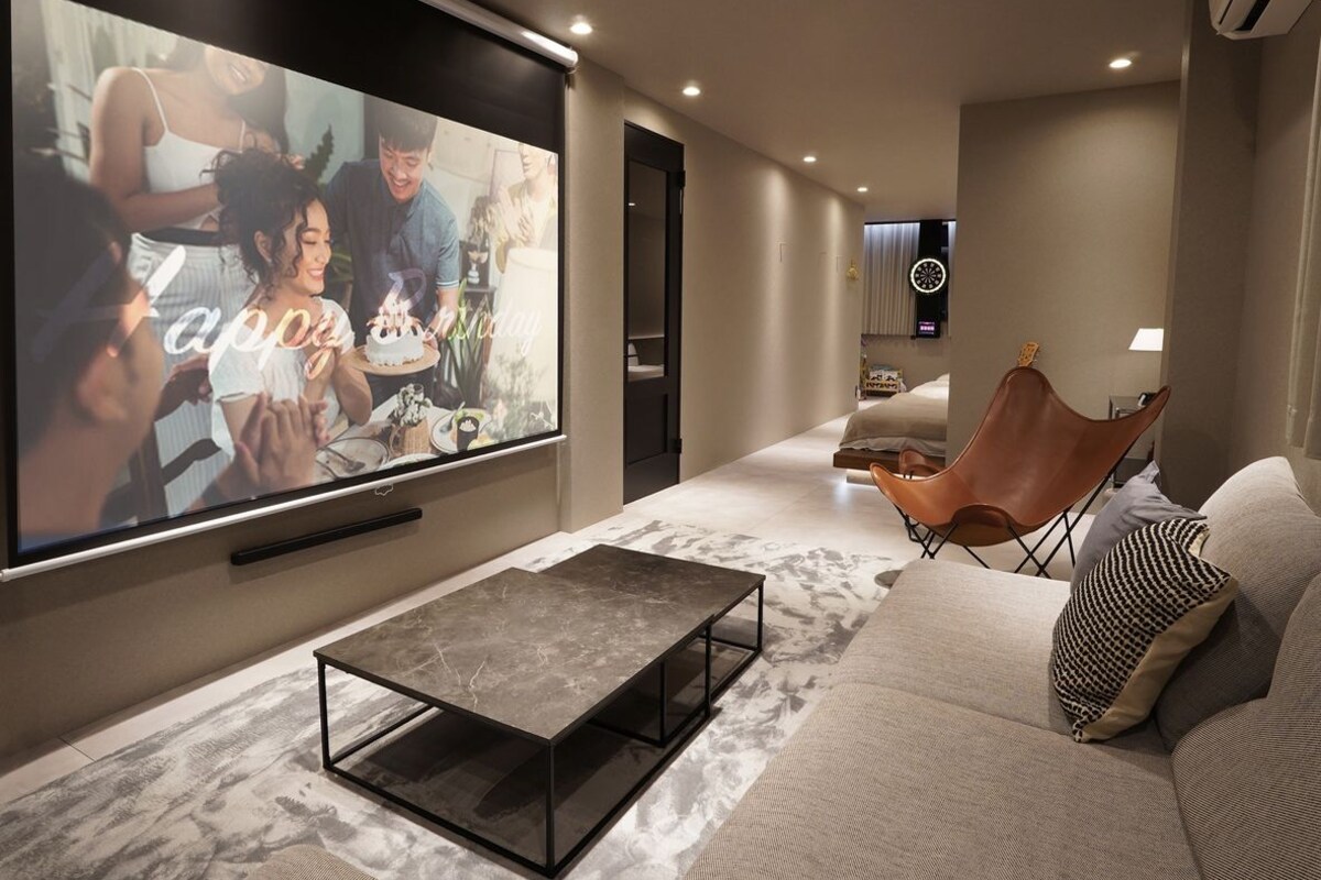 Ein modernes Wohnzimmer mit einem großen Flachbildfernseher, einer Couch, einem Couchtisch und einem Sessel.