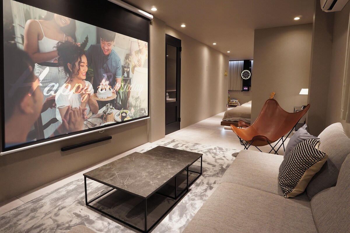 Ein modernes Wohnzimmer mit einem großen Flachbildfernseher, einem мраморном журнальном столе, einem Ledersessel und einem Sofa mit gemusterten Kissen.