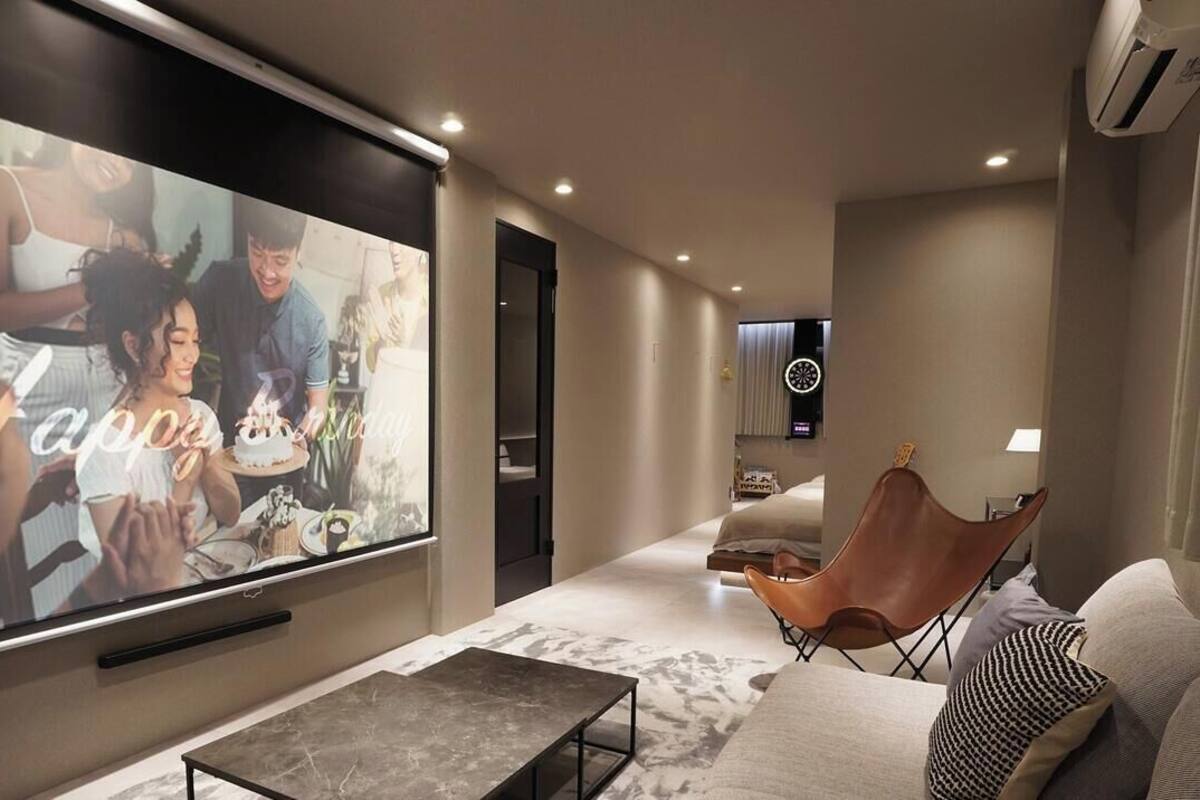 A modern living room with a large flat-screen TV, a leather armchair, a sofa, and a coffee table.